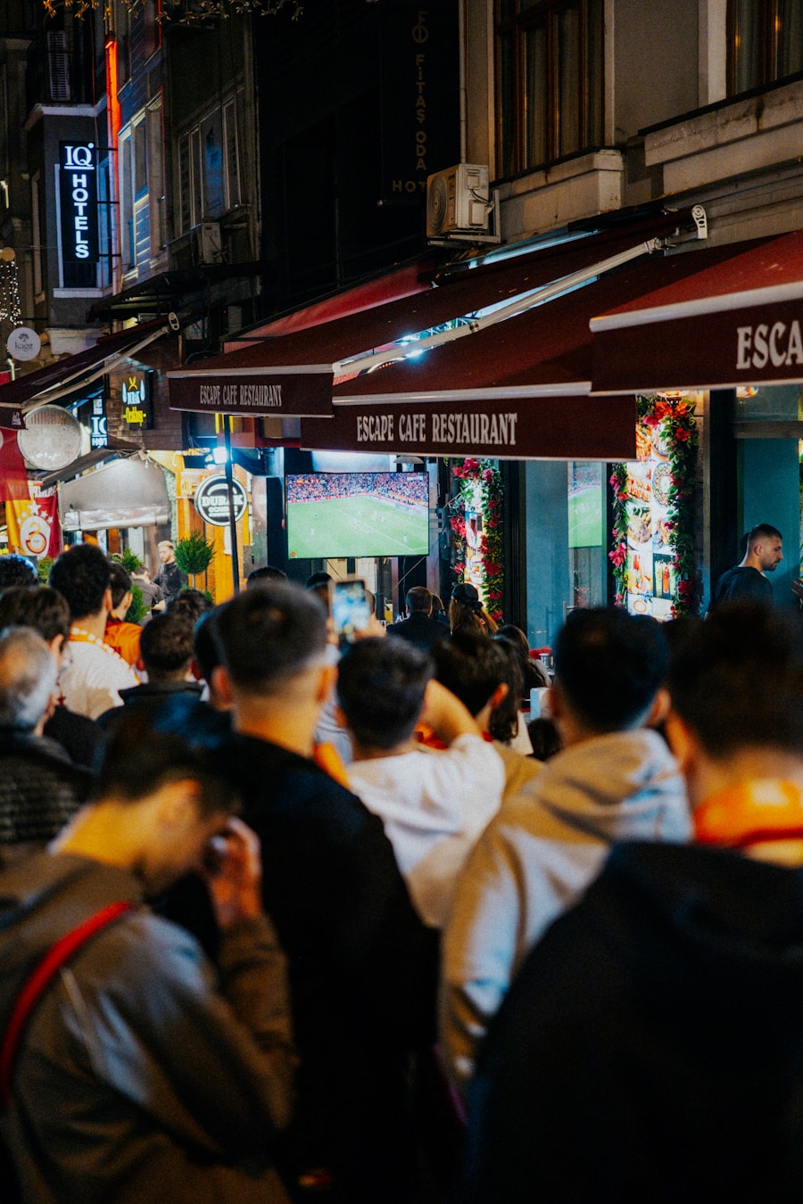 A street crowd watching a soccer match on an outdoor screen at night