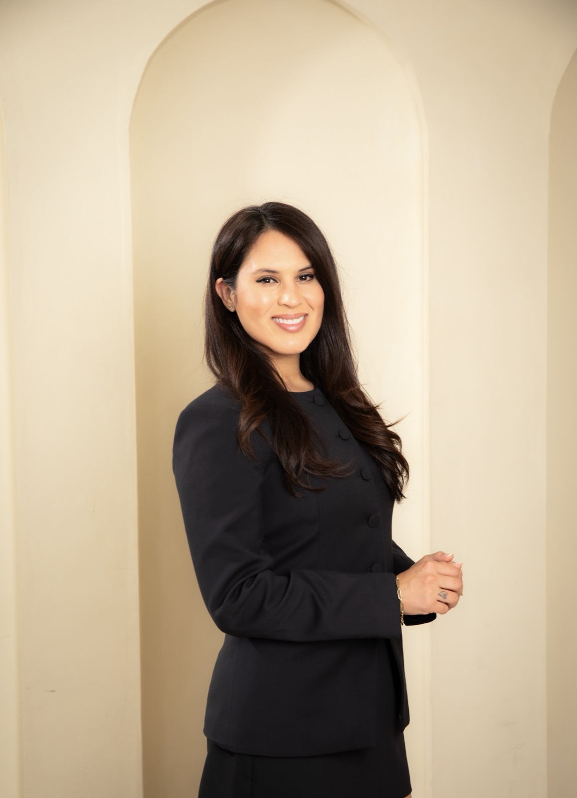 Thalia Nagda, realtor and designer, in a black dress against a cream arched wall